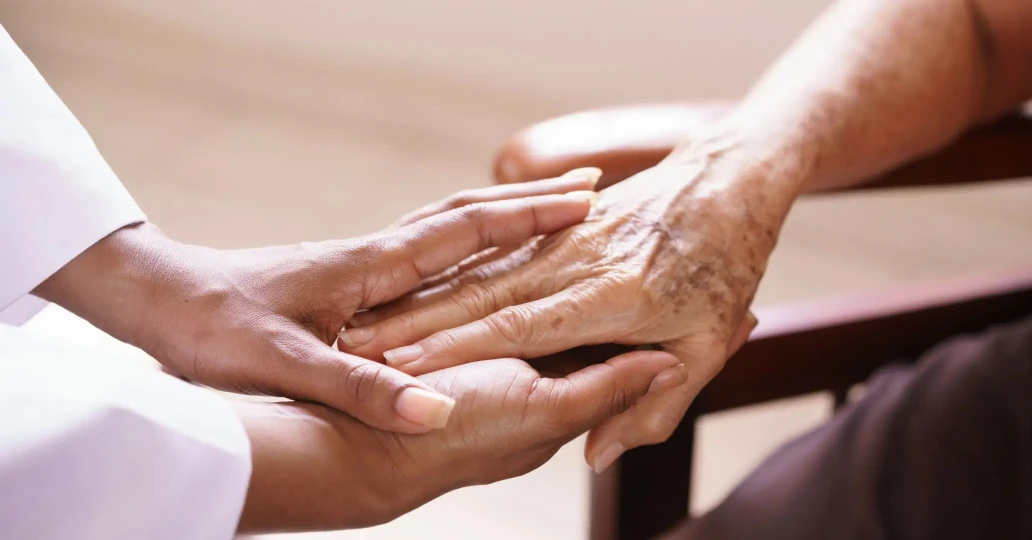 Close-up image of a carer's hands gently holding the hands of an elderly person, symbolizing support and compassion in elderly care.