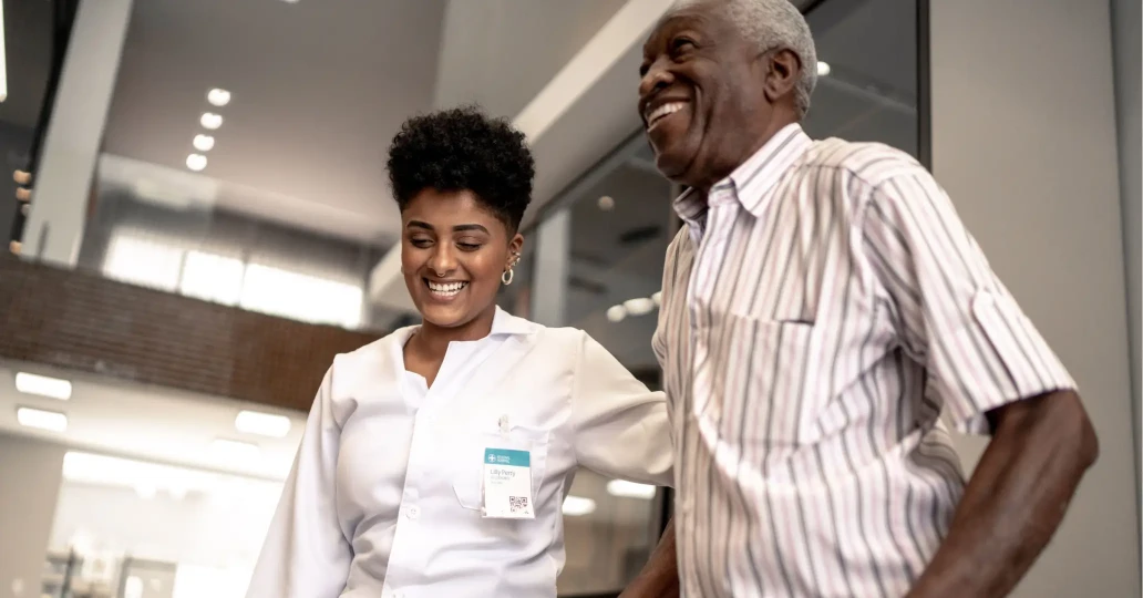 A joyful interaction in a hospital setting between a young female nurse and an elderly male patient, both smiling as they walk through a hallway, highlighting compassionate care.