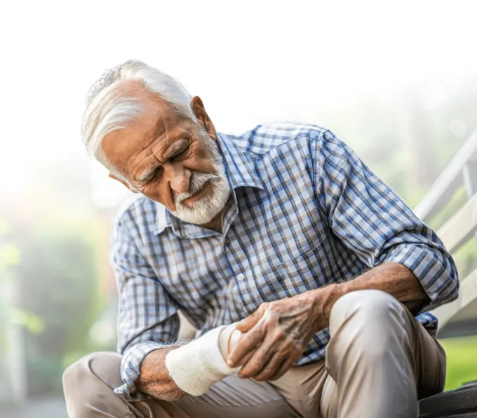 Elderly man sitting on a park bench, examining a bandage on his wrist, showing a moment of concern or pain