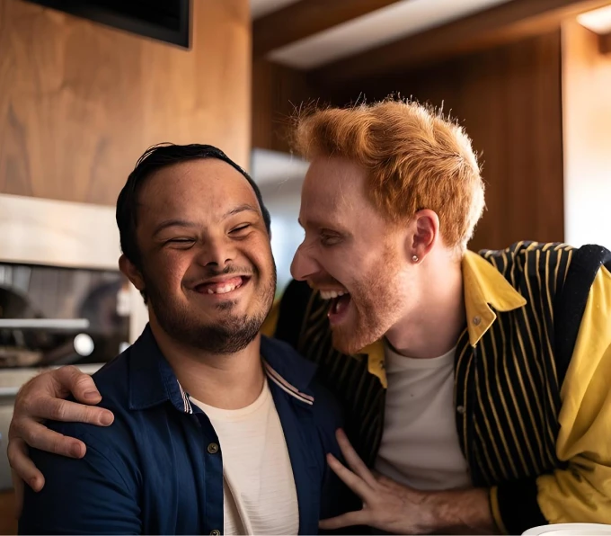 Two friends sharing a joyful moment in a cozy kitchen setting, one man embracing the other and laughing, expressing happiness and close companionship.