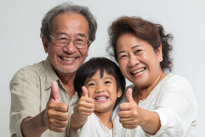 Smiling grandparents and grandchild in white clothing giving thumbs up together